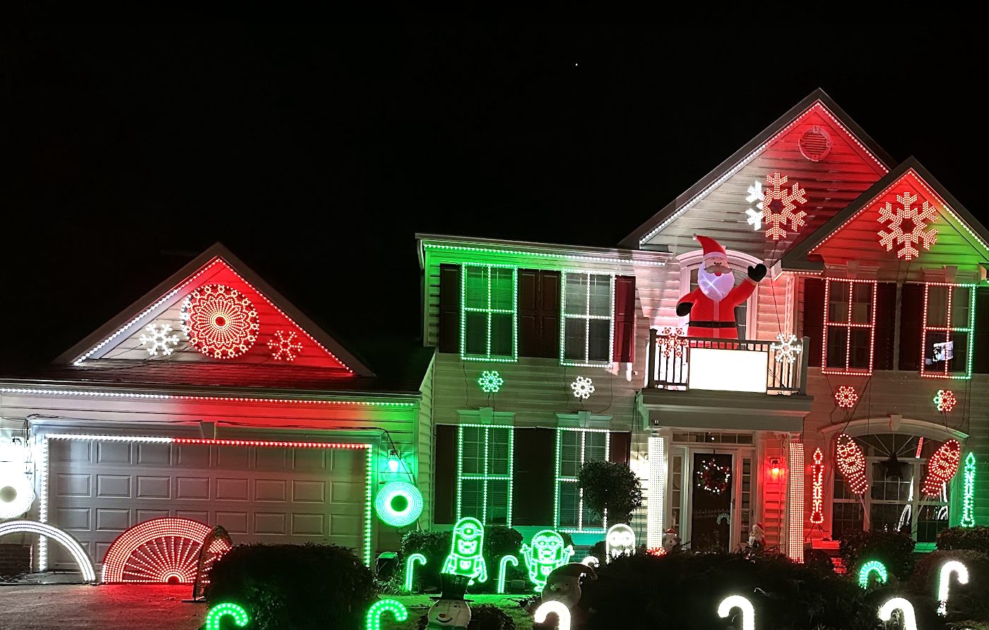The house at Christmas 2022 in red, green, and white: pixel snowflakes on the gables, glowing candy canes and minions on the lawn, and a waving Santa on the balcony